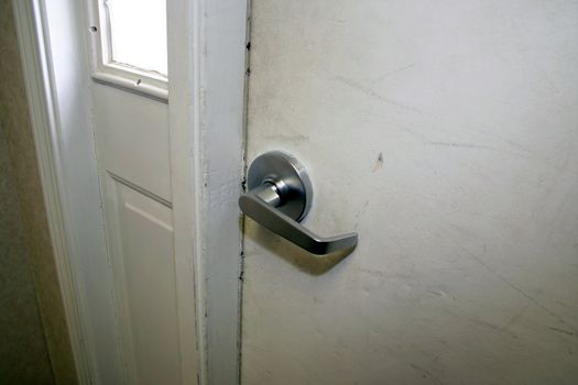 A door handle on a white door - the finish on the door is a little beat up.