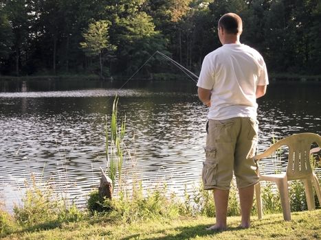 A lone fishermen fishing in a rural pond.