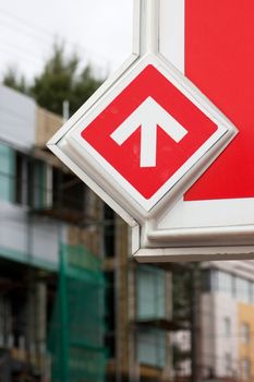 Closeup view of road sign. White arrow over red background. One direction.