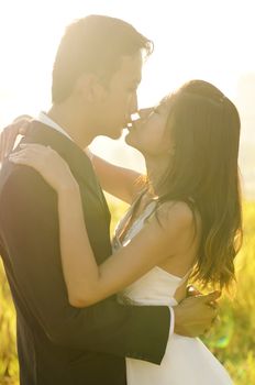 Bride and groom kissing in the park, back-lit with lens flare in the morning.
