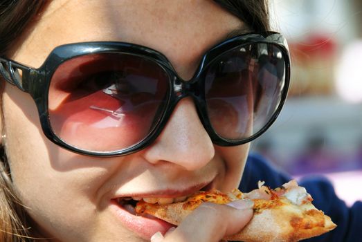 smiling teenage girl in sunglasses eating pizza closeup
