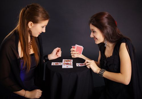 Two girls friends engaged in fortune-telling cards on a dark background