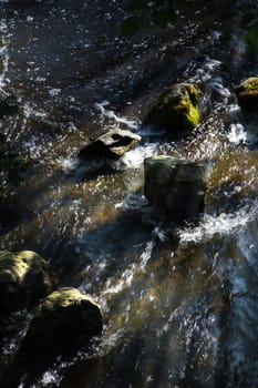 Sunrays in the morning shining over boulders and running water 