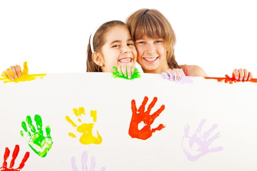 Two smiling little girls holding white sheet with colourful hand prints