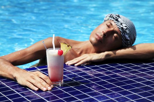 The man with a cocktail in pool (glass in focus, the rest is dim)