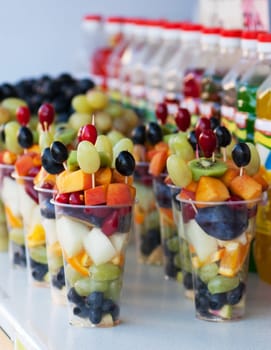 Fruit pieces (grape, kiwi, peach, apple, orange) in plastic cups