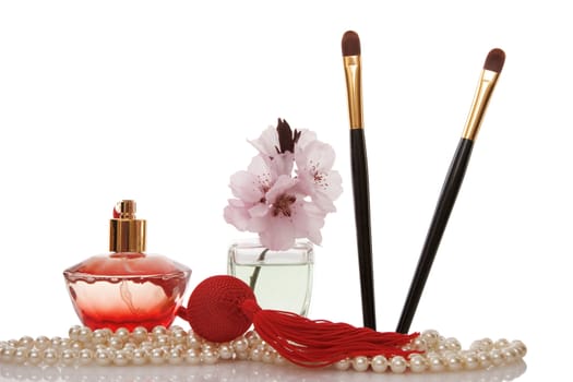 Pearls beads, perfume, two cosmetics brush and cherry flower on white background