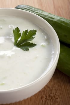 Bowl of fresh cucumber soup made with yogurt, whole cucumbers to the side.