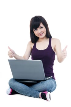 Portrait of a cute young female sitting on floor with laptop, giving thumbs up sign over white background.
