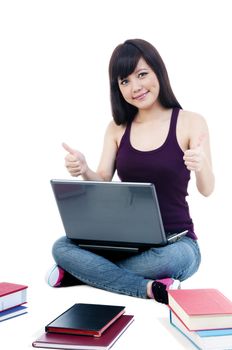 Portrait of an attractive female student sitting on floor with laptop, giving thumbs up sign over white background.