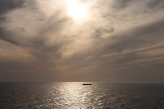 A silhouette of a lone ship at sea against the setting sun.