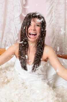 Happy woman playing with feather and down stuffing and laughing.