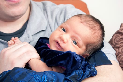 A cute newborn baby girl being held by her dad with a smile on her face.