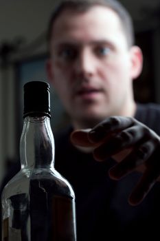 A man struggling with alcoholism reaches for his bottle of liquor. Shallow depth of field.