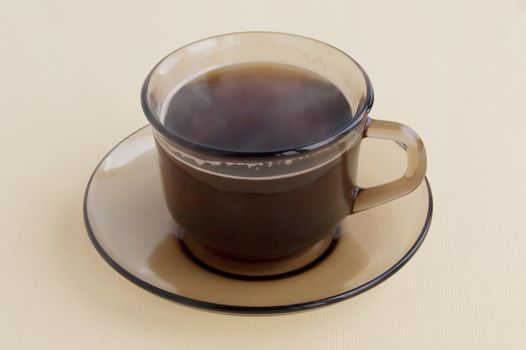 Cup and saucer made of brown glass with hot coffee in isolation at the beige background of light material