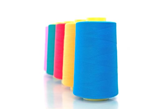 A number of bobbins and thread of blue, yellow, red, green and pink in isolation on a white background
