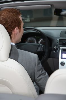 A young man in a grey suit driving a luxury convertible car