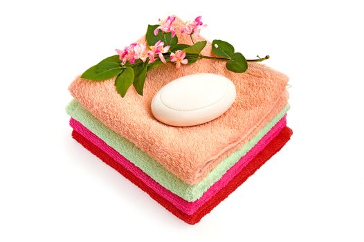 White soap, a branch with pink flowers and green leaves, a pile of towels on a white background