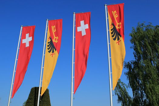 Swiss and Geneva canton flags moving in the wind and deep blue sky