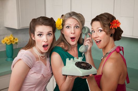 Three surprised women holding a rotary telephone in a kitchen