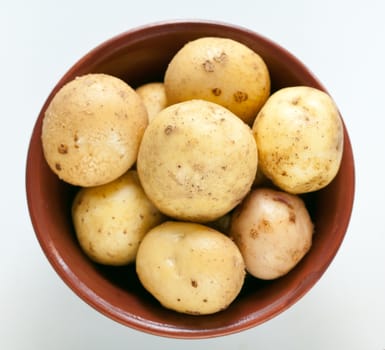 Fresh potatoes unpeeled potatoes in clay bowl, top view. Light background