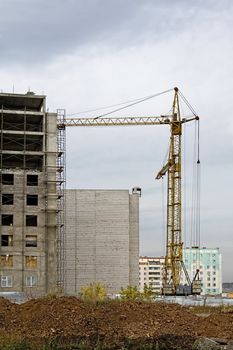 Building under construction, crane, at home against the backdrop of an overcast sky and gray clouds