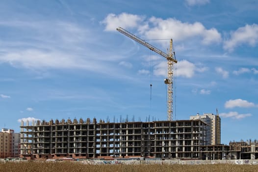 Building under construction, crane against the blue sky and clouds