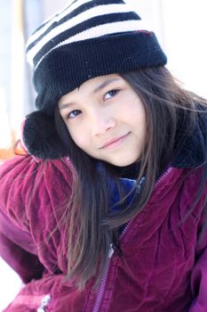 Spunky little girl wearing her full winter attire standing hand on hip outdoors in winter with a challenging expression.