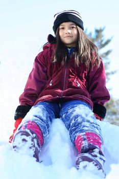 Young girl in winter attire playing on top of snow hill. Part Scandinavian, part asian descent.
