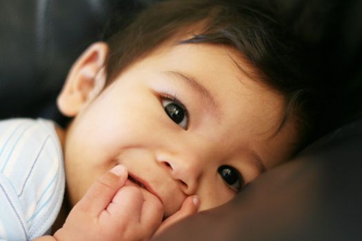 Baby boy happily sucking fist on couch