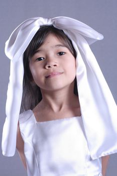 Cute little girl playing dress up with satin bow on head. Part asian, scandinavian background.