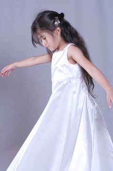 Beautiful little girl in white satin gown twirling playfully. Part Asian, Scandinavian background.