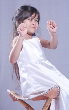 Cute little girl in white satin dress playing with her hands. Part asian, scandinavian background.