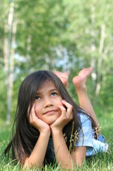 Child lying on grass with a thoughtful expression. Part asian, scandinavian background.