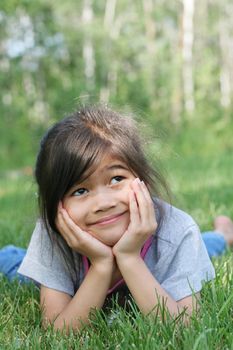 Child lying on grass with a thoughtful expression. Part asian, scandinavian background.