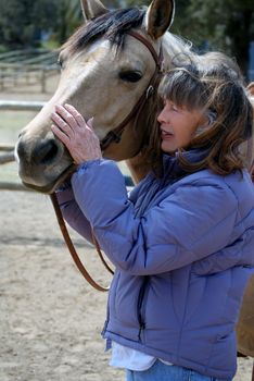 Vertical image of a Baby Boomer era woman showing affection to her horse.