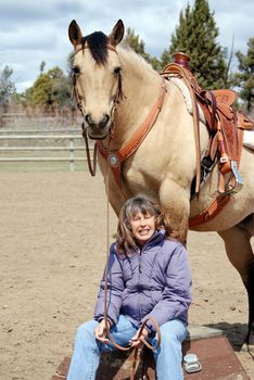 Vertica image of a pretty dun quarter horse standing on a circus platform while her owner sits at her feet, smiling into the camera.