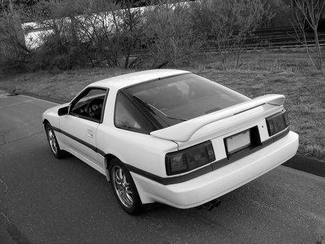 a japanese sports car captured at a cool and artistic angle, parked on the side of the street near alongside some railroad tracks - black and white