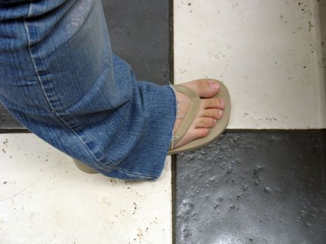 a flip flop on a girl's foot, standing on a ceramic tile floor.