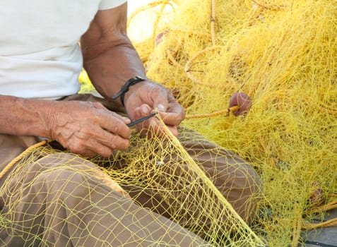 A fisherman mending his yellow fishing net on his boat in a Greek island.