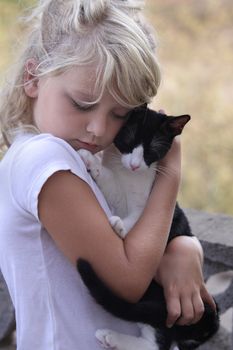 A young girl is sweetly hugging her black and white cat. Both have their eyes closed. 
