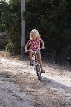 A young girl is struggling with learning to ride her bike. She is very concentrated