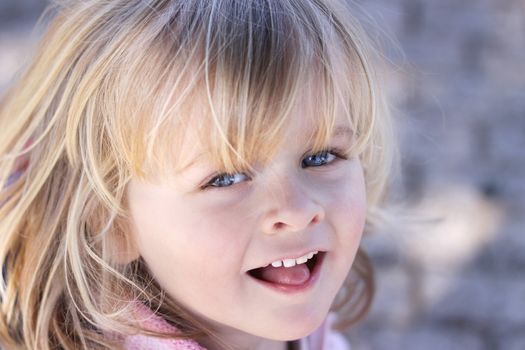 Closeup of a beautiful little girl with sparkling eyes and a cheeky smile. Background out of focus. Positive, happy feeling