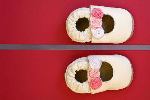 Beautiful tiny cream coloured baby princess shoes with roses, photographed on a red chair