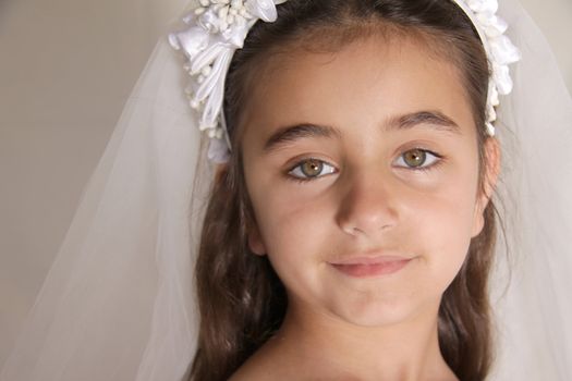A horizontal head shot of a beautiful young girl, dressed up in veil and a hairband for her holy communion. She has long brown hair and beautiful mixed coloured eyes. Content, peaceful feeling