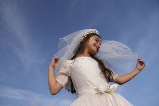Happy girl in holy communion dress against blue skies