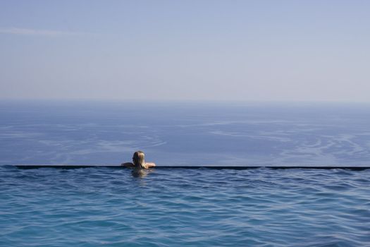 A girl resting at the end of a stunning infinity pool. Space for text