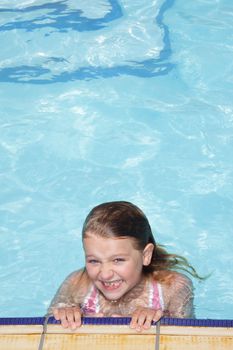 A smiling 8+ year old girl hanging on to the edge of a swimming pool