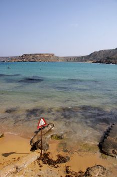 A roadsign warning for falling rocks set up on a beautiful quiet beach on the island of Malta, Europe