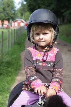 Close up of a little 4 year old girl sitting on a pony with a riding helmet